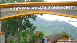 Un arco de piedra con la inscripción "Kawasan Wisata Songgoriti", señalando un destino turístico.