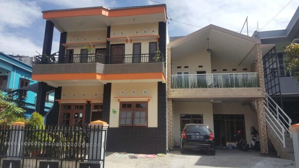 Un edificio residencial de dos plantas con un balcón en el piso superior, un coche estacionado al frente y una escalera que conduce a la entrada.