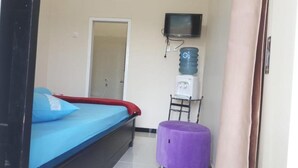 Una habitación con cama, dispensador de agua, televisor y un taburete pequeño morado.