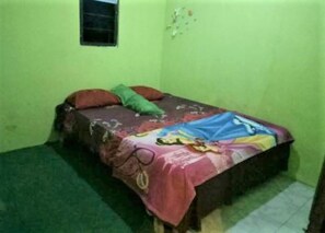 A small, single-bed room with a green wall, a window, and a colorful bedspread.