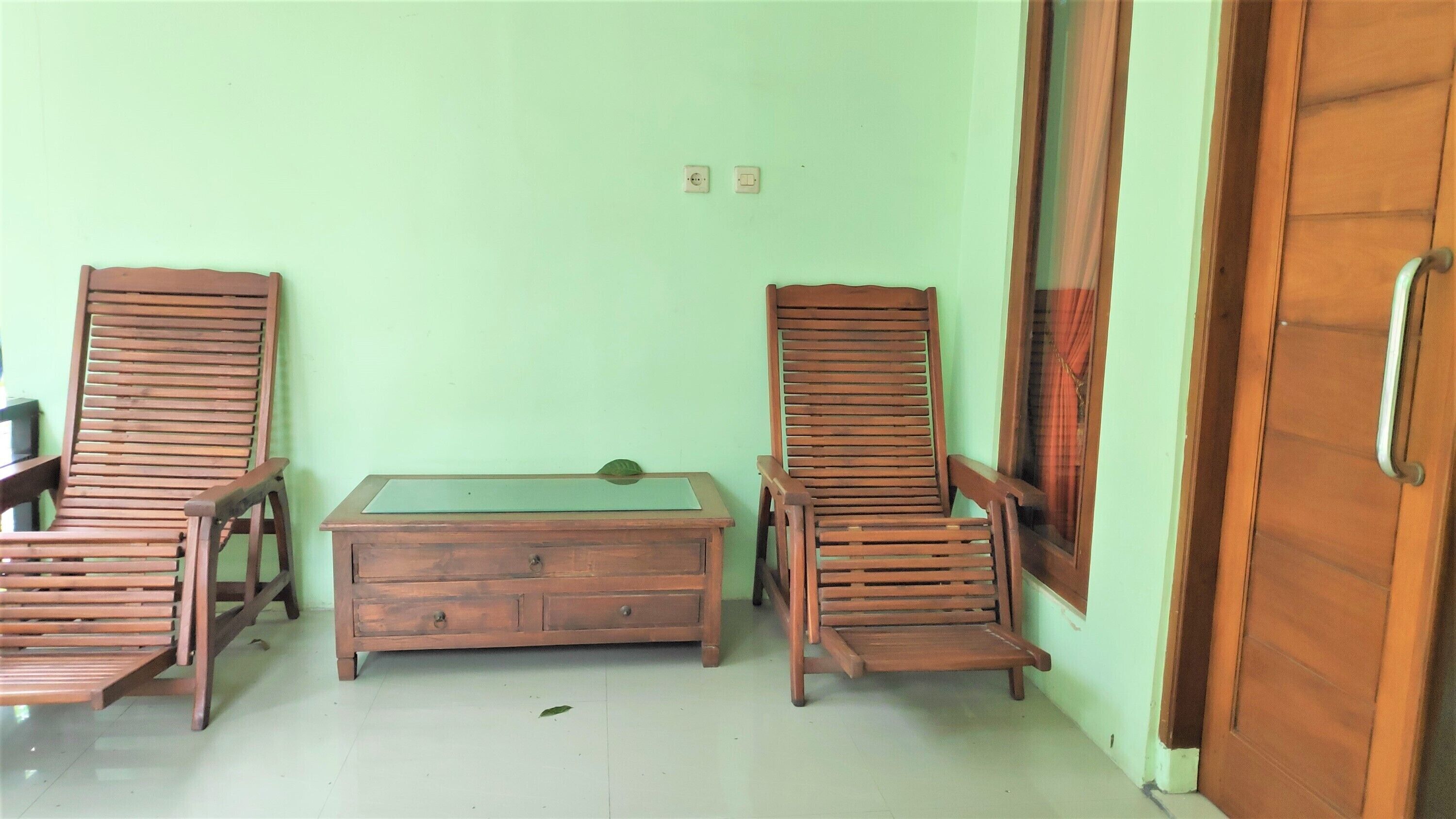 Een kamer met twee houten stoelen, een klein houten tafeltje en een deur.