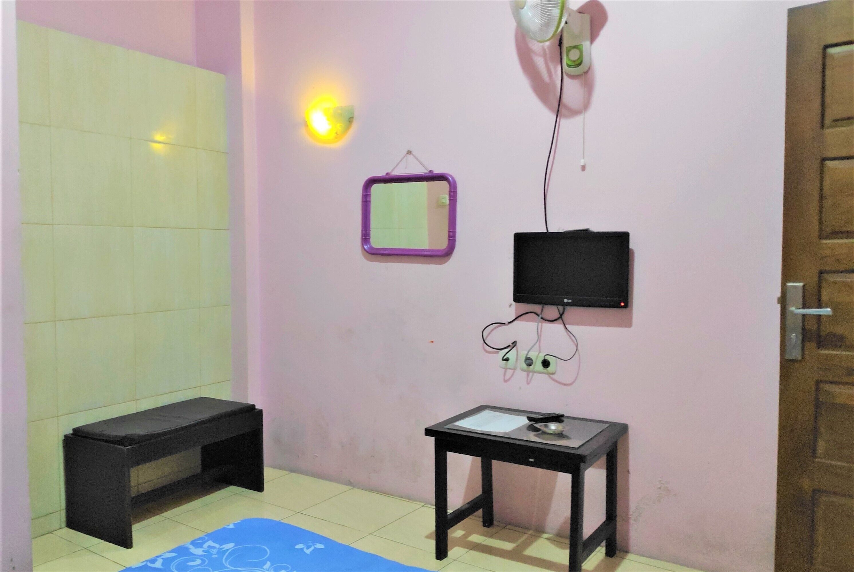 Una habitación pequeña con una banca, una mesa con espejo, un televisor y un calentador de pared.