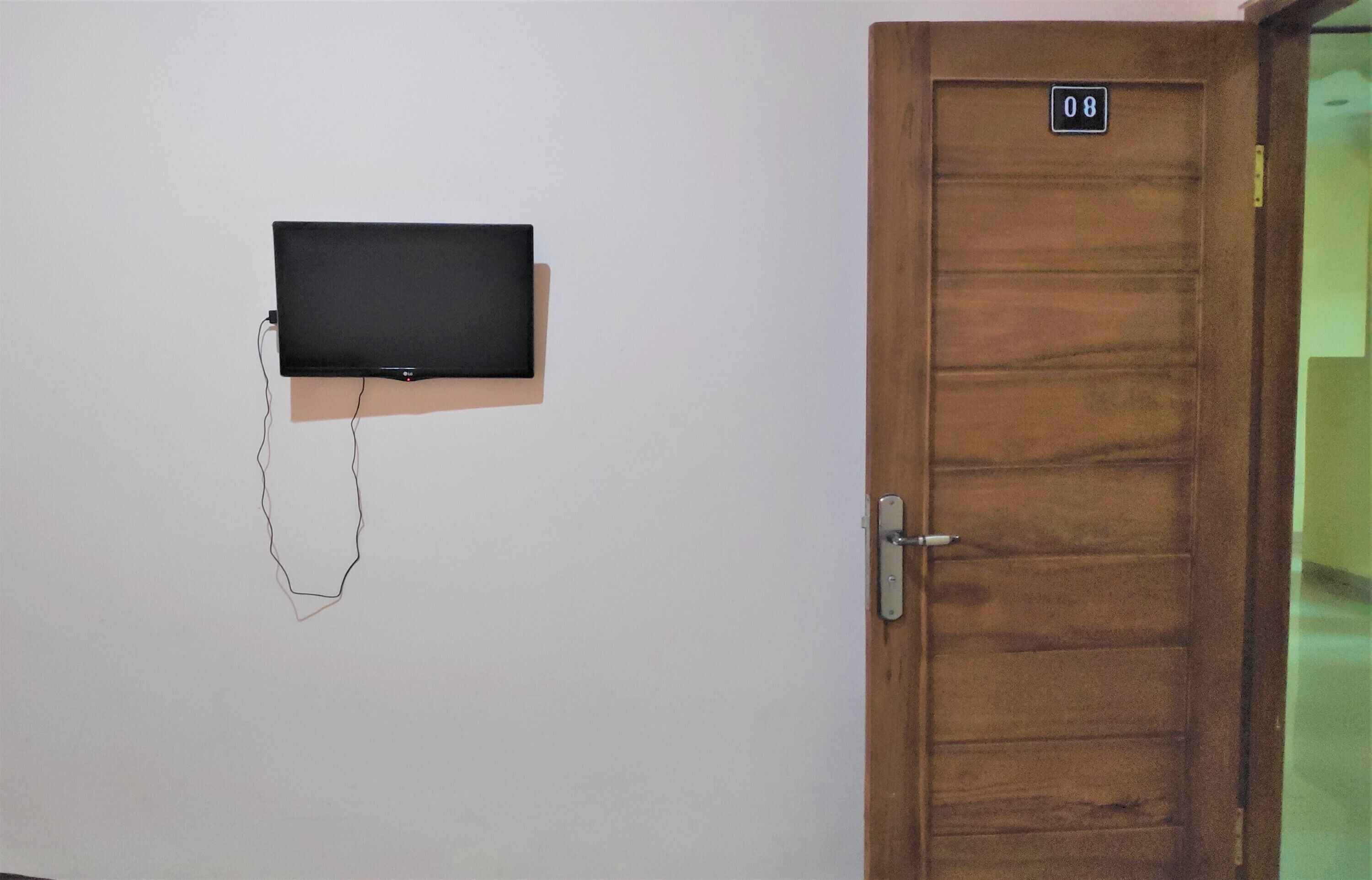A room with a wooden door marked with the number 08, a television mounted on the wall, and a door handle.