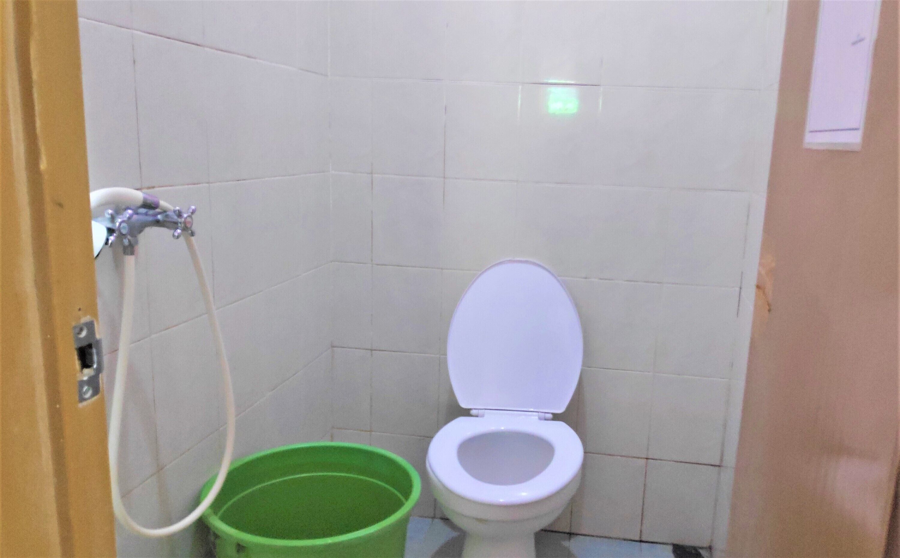 A small bathroom with a toilet, a green bucket, and a shower hose.