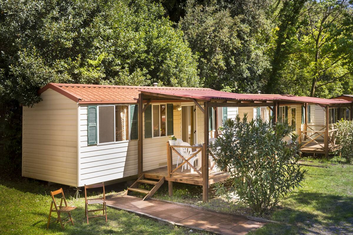 A row of small, single-story cabins with wooden decks and green shutters, surrounded by lush greenery.