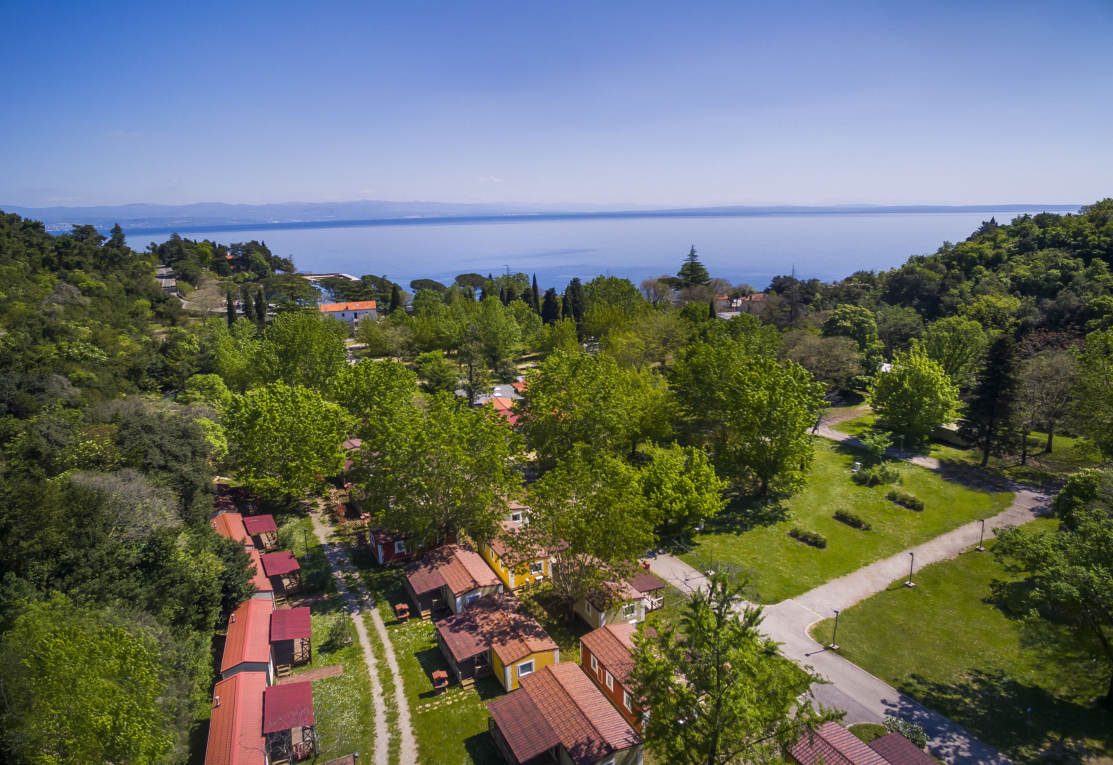 An aerial view of a residential area with houses, a clear sky, and a body of water in the distance.