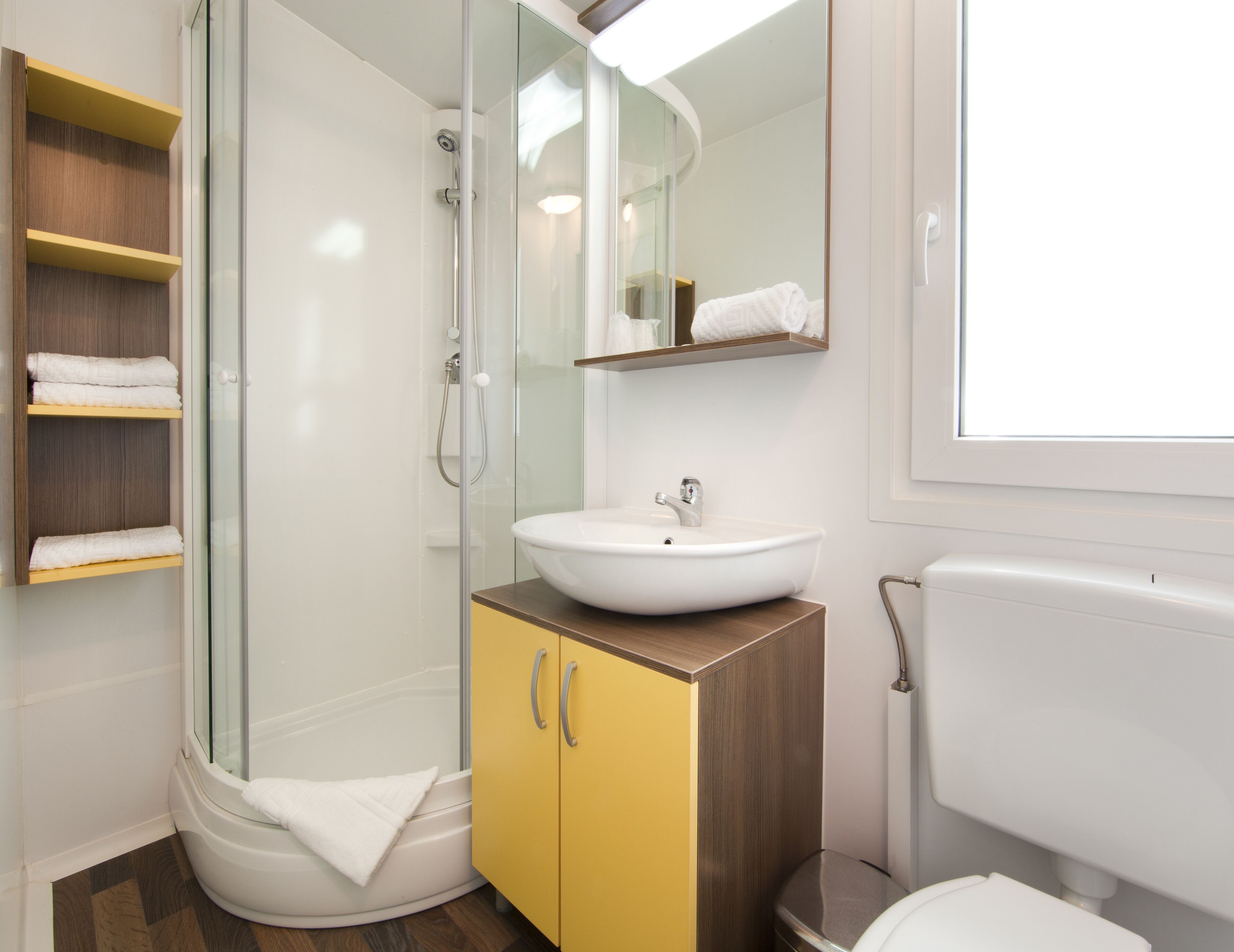 A modern bathroom with a glass-enclosed shower, a white sink, and a yellow cabinet.
