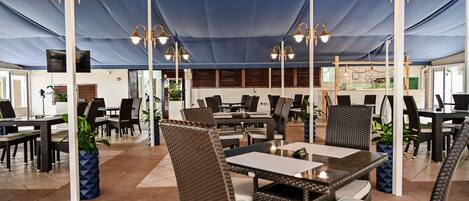 An indoor patio area with wicker furniture, tables, and chairs under a blue canopy.