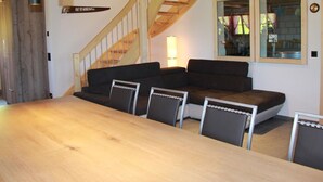 Un área de comedor moderna con una mesa de madera, sofás tapizados en negro y una escalera con barandillas de madera.