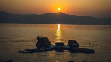 A sunset over a calm body of water with mountains in the background and floating platforms with seating.