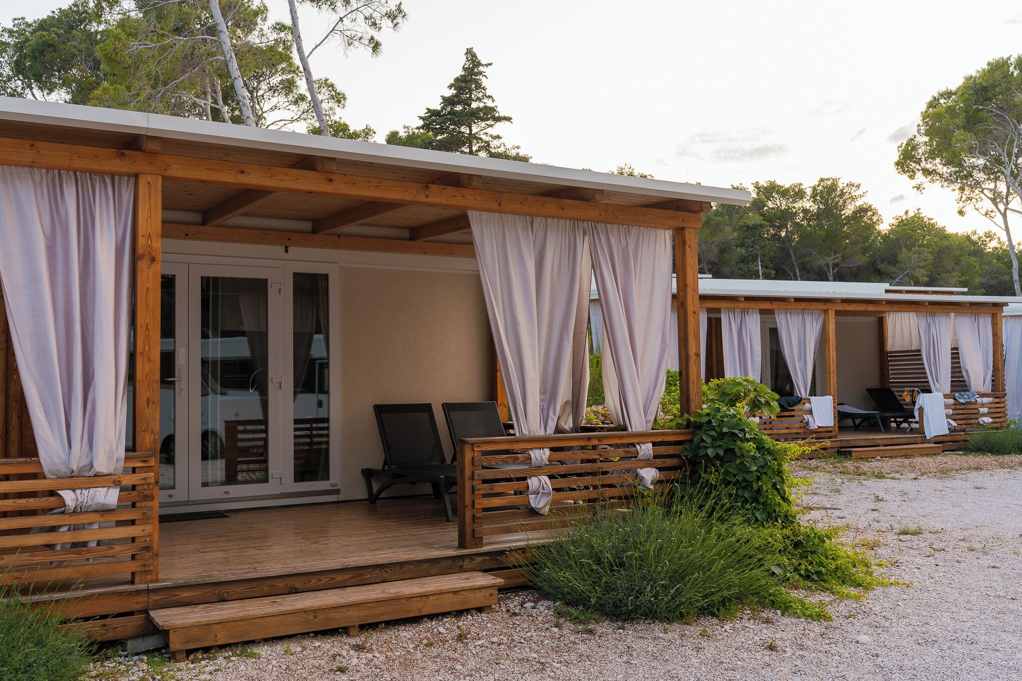 A wooden cabin with a covered porch, two lounge chairs, and a bench.