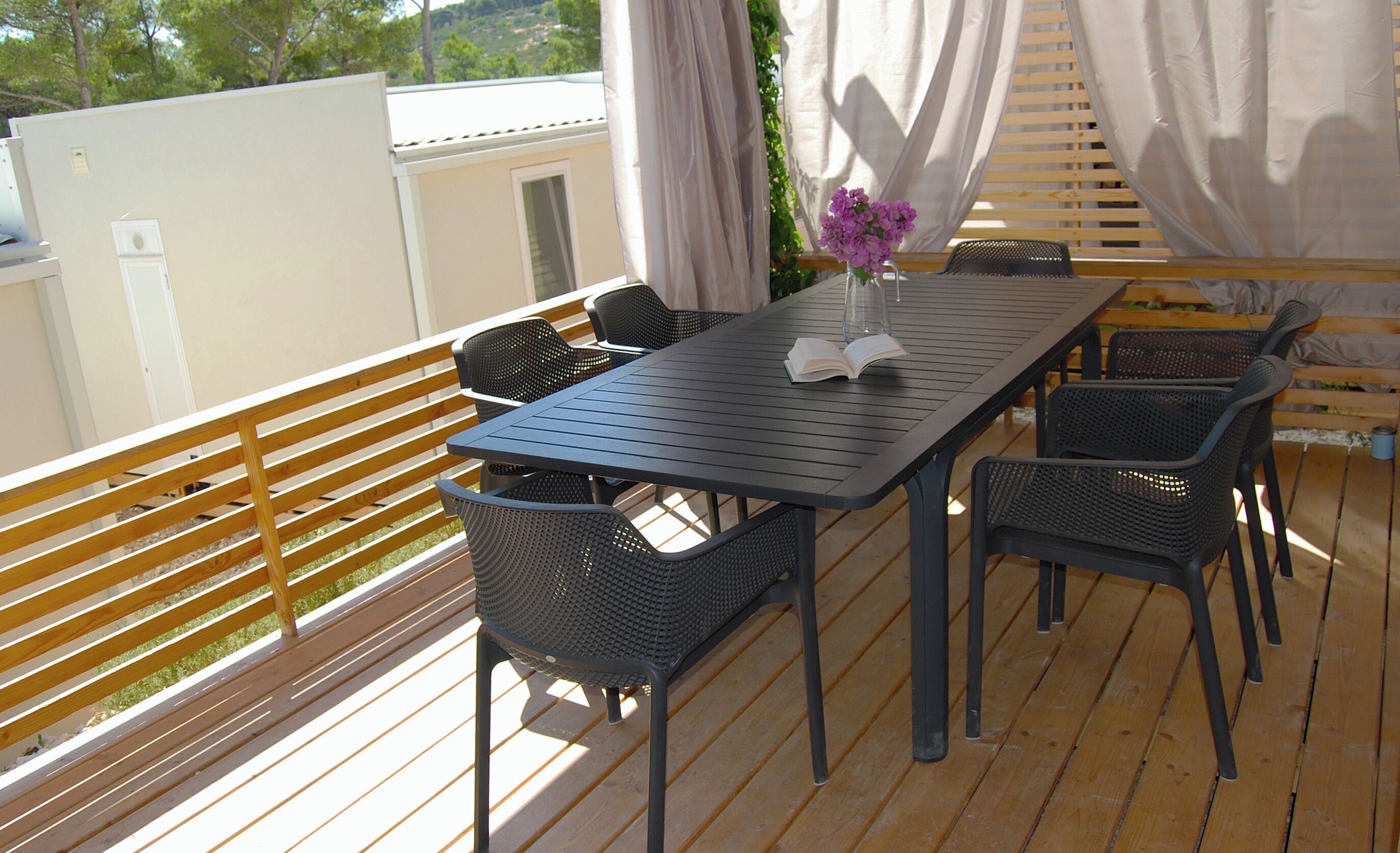 A covered outdoor seating area with a table and chairs, a book, and a vase with flowers.