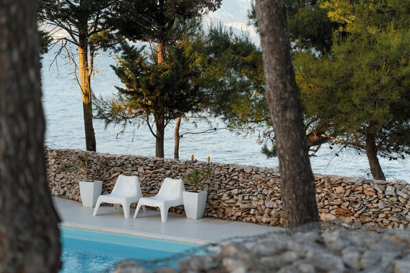 A poolside area with white lounge chairs and a stone wall. - Boutique Camping Bunja (Supetar)