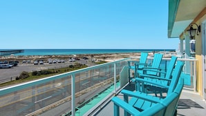 Un balcon avec des chaises turquoise donnant sur une plage et un espace de stationnement.