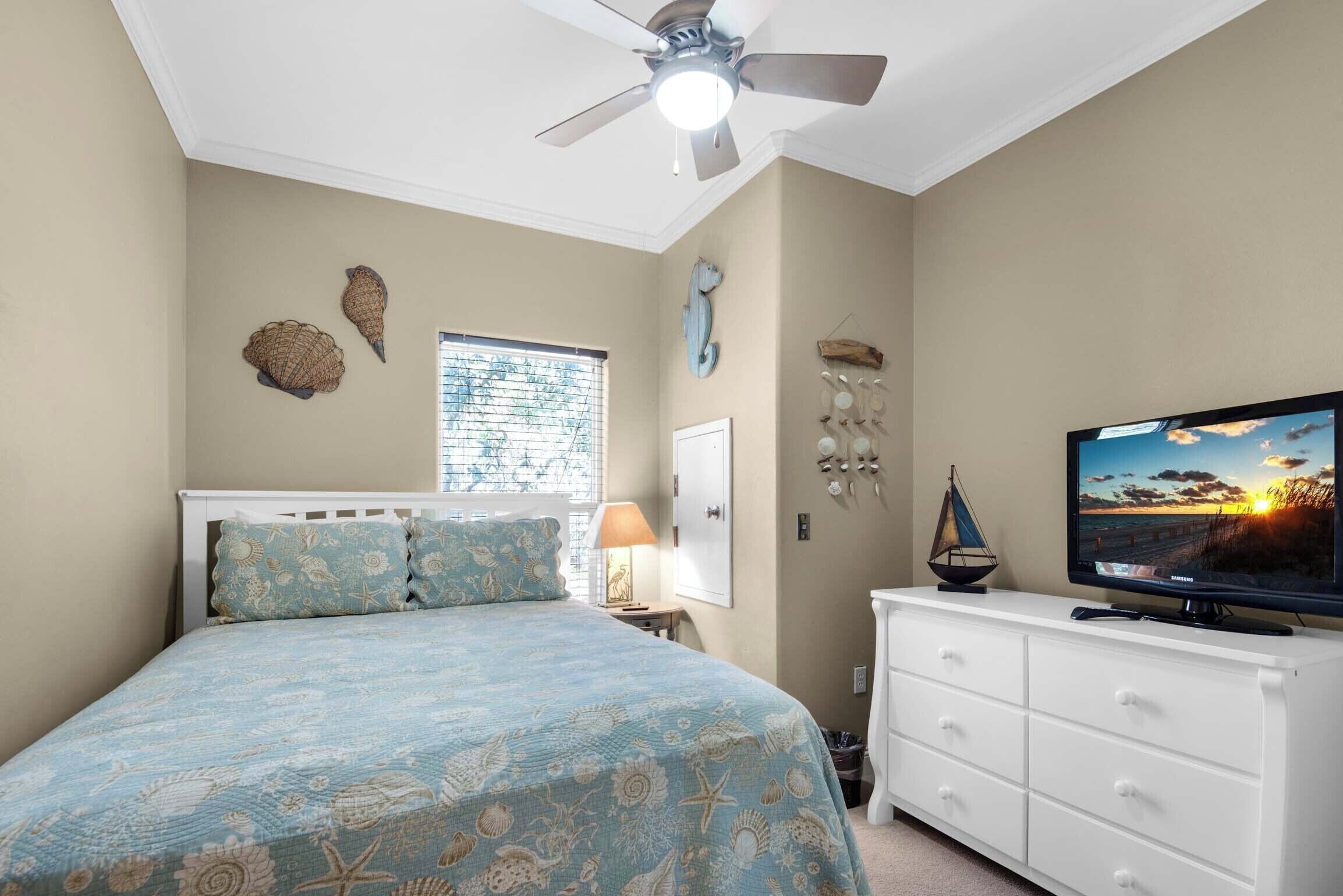 Een slaapkamer met een bed, een televisie, een plafondventilator en decoratieve wanddecoratie.