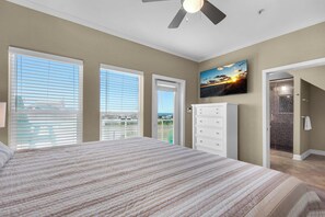 Relax in this serene bedroom with a large bed, wall-mounted TV, and convenient access to a bathroom with a glass shower.