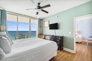 A bedroom with a large bed, a ceiling fan, a TV, and a view of the ocean. - Beach Service Included | Gulf-Front 15th Floor Condo | Stunning Sunset Views (Panama City Beach)