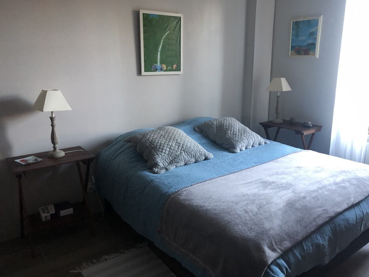 A bedroom with a bed, two pillows, a nightstand, a lamp, and two wall art pieces.