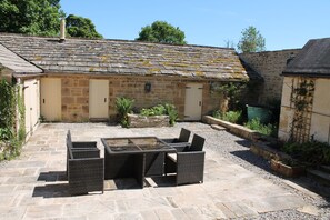Relax on the patio with a glass-top table and four wicker chairs, surrounded by lush greenery.