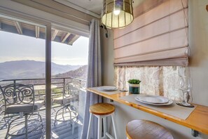 Varanda com mesa posta para refeições, uma cadeira e vista para as montanhas.