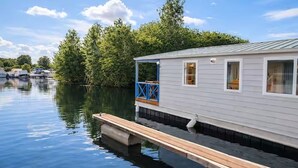 A houseboat docked on calm water with a wooden deck and a blue railing.