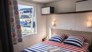 A bedroom with a bed, striped bedding, a nightstand, a wall-mounted shelf, and a window with a view of boats.