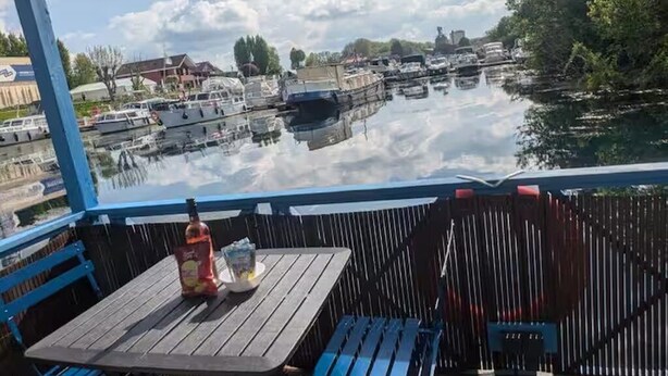 A view from a covered outdoor area with a table and chairs, overlooking a marina with boats and buildings in the background.