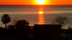 A sunset over a body of water with silhouettes of palm trees and buildings in the foreground. - Rent room Nontiscordardimè (Civitanova Marche)