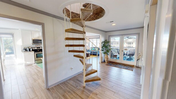 Un amplio salón con una escalera espiral, una cocina equipada con electrodomésticos modernos y un balcón con mobiliario de exterior.