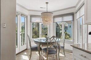 A dining area with a round glass table, white chairs, and a chandelier.