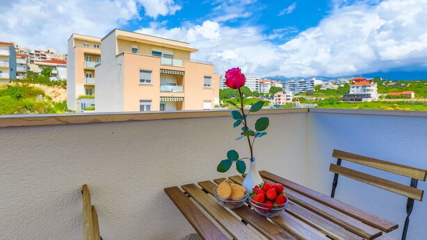 A balcony with a wooden bench, a vase with a single rose, and bowls of strawberries and cookies. - Spacious studio with balcony, close to the Znjan beach (Split)