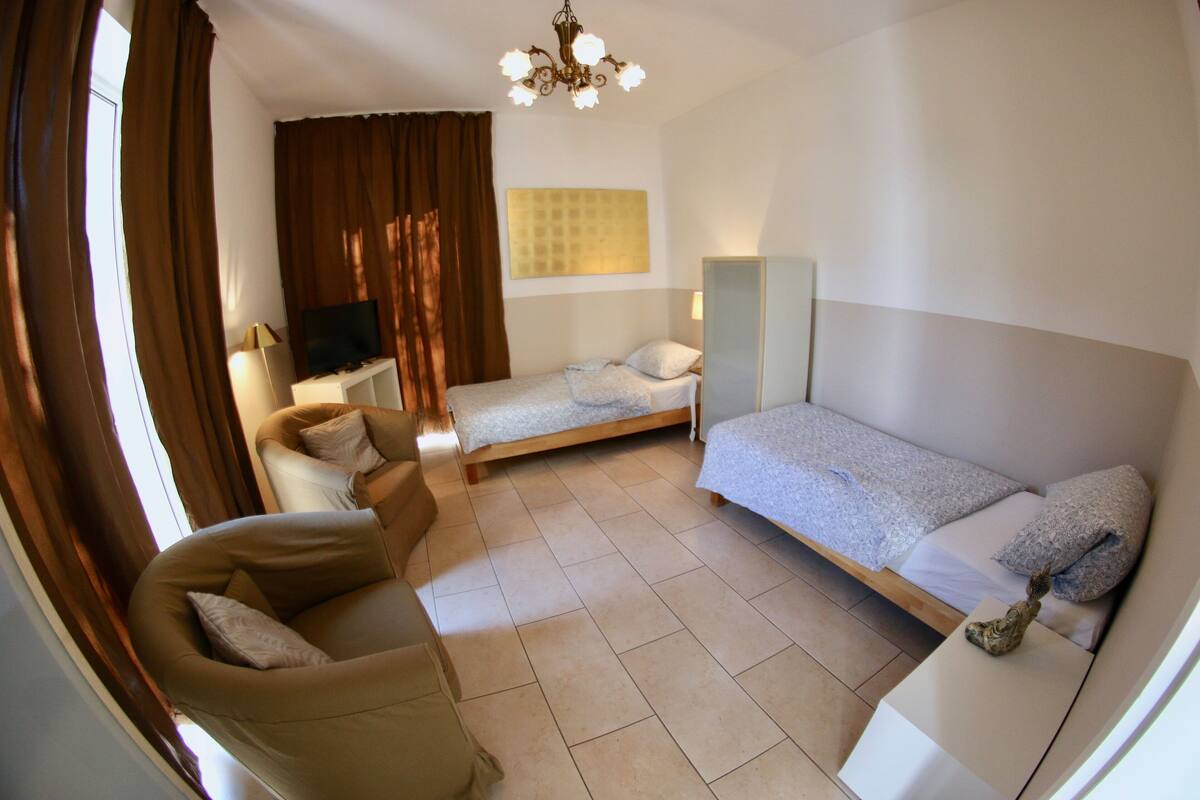 A hotel room with a sofa, two single beds, a TV, and a mirror.