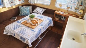 Interior acogedor de una autocaravana con cama, una mesita con comida y bebidas, una planta y un baño.