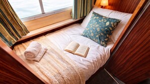 Una cama acogedora con un libro, una toalla enrollada y una ventana con cortinas.