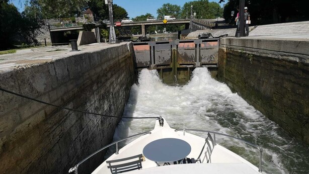Un bote navegando por una vía fluvial estrecha, con un puente al fondo.