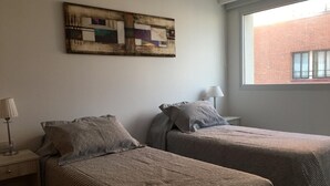 A room with two beds, a nightstand, a lamp, and a window with a view of a brick building. - Tranquility and peace, in Maires la Isla (Mar del Plata)