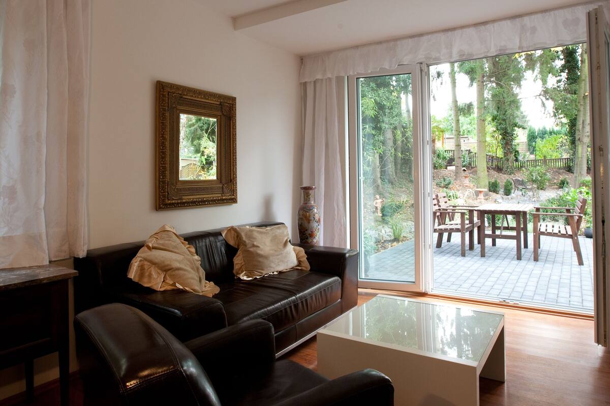 A living room with a black leather sofa, a glass coffee table, a framed picture on the wall, and a sliding glass door leading to an outdoor patio.
