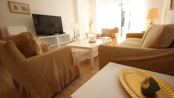 Ein Wohnzimmer mit beigen Sofas, einem weißen Couchtisch, einem Flachbildfernseher und einer Lampe.