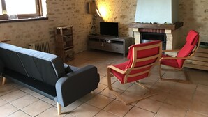 Una sala de estar con pared de piedra, chimenea, sofá, televisor y una butaca roja.