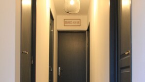 Un pasillo estrecho con piso de madera, puertas oscuras a ambos lados y una lámpara en el techo.