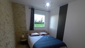 Un dormitorio con cama, ventana con cortinas, lámpara de noche y pared con textura.