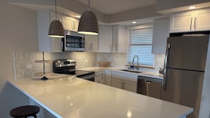 Une cuisine moderne dotée d’un grand îlot central, d’appareils électroménagers en acier inoxydable, de luminaires suspendus et d’un dosseret en carreaux disposés en motif chevrons.