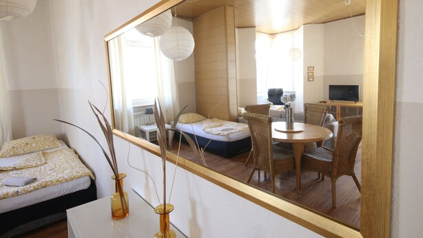 A bedroom with a bed, bedside table, and a mirror reflecting a dining area with chairs and a table. - a-domo Apartments Oberhausen - Budget Apartments & Flats - short & longterm - single & grouptravel (Oberhausen)
