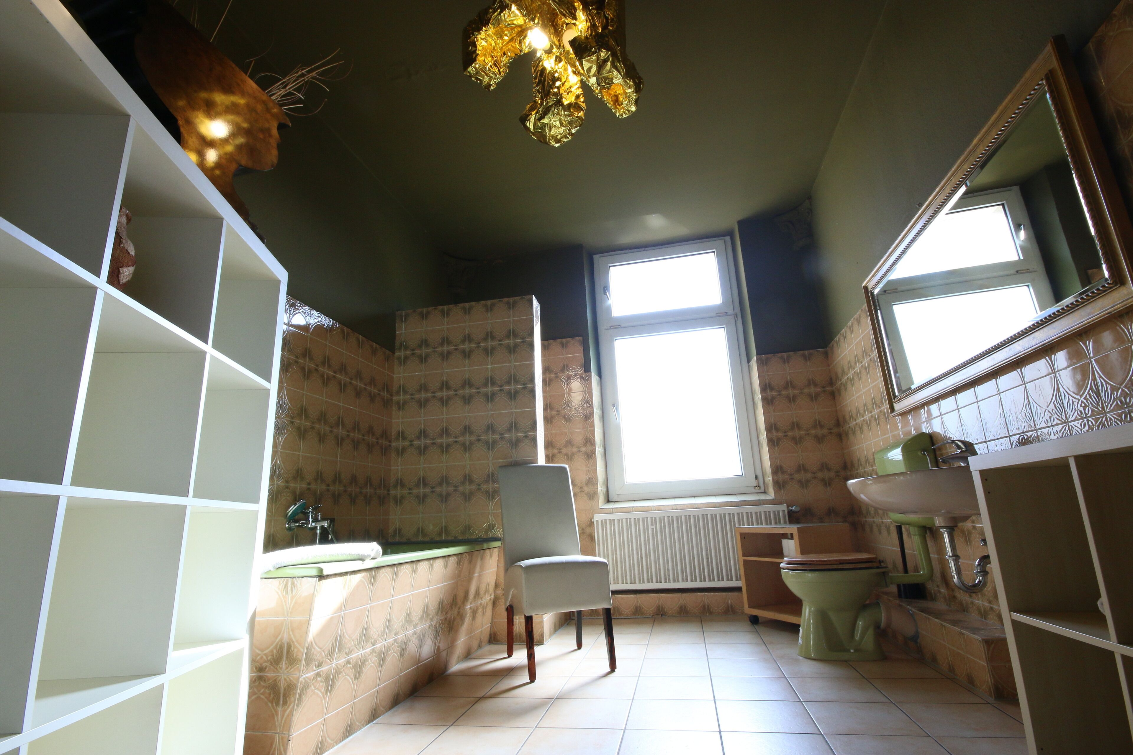 Een badkamer met betegelde vloer, een stoel, een wastafel, een toilet en een raam.