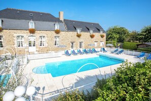 A stone building with a swimming pool, lounge chairs, and a clear blue sky.
