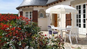Ein Haus mit einer Stein-Fassade, einem Ziegeldach und einer Terrasse mit Tisch und Stühlen.