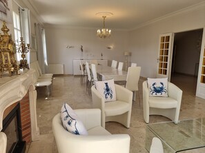 A spacious room with a dining table, white chairs, a fireplace, and a chandelier. - la Villa des Longchamps (Saint-Jouan-des-Guérets)