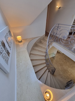 A spiral staircase with a metal railing, a wall-mounted light, and decorative wall art.