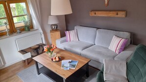 A cozy living room with a grey sofa, a wooden coffee table with magazines, a lamp, and a deer skull on the wall. - Ferienwohnung bis 2 Personen, Erdgeschoss, Terrasse (Grassau)