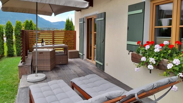 A patio with two lounge chairs, a table, and a covered umbrella. - Ferienwohnung bis 2 Personen, Erdgeschoss, Terrasse (Grassau)